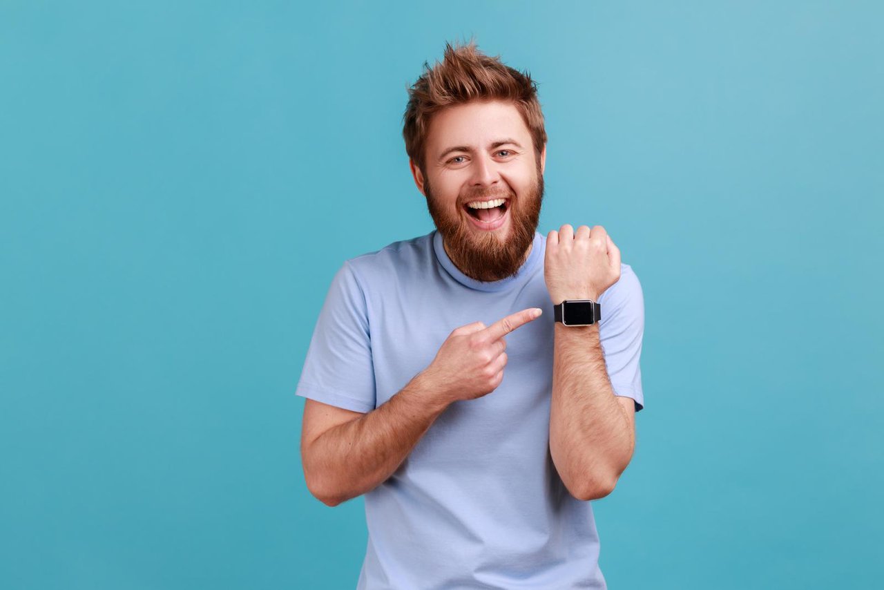 man with open mouth and satisfied expression, pointing with finger ar smartwatch and laughing.