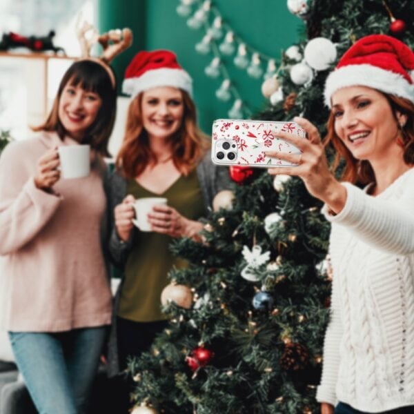 Etui do iPhone 15 Pro, cukierki świąteczne (3) Przyjaciele robią selfie przy choince świątecznej.