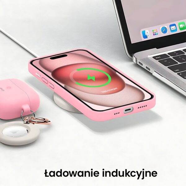 Różowy smartfon na ładowarce indukcyjnej obok laptopa.