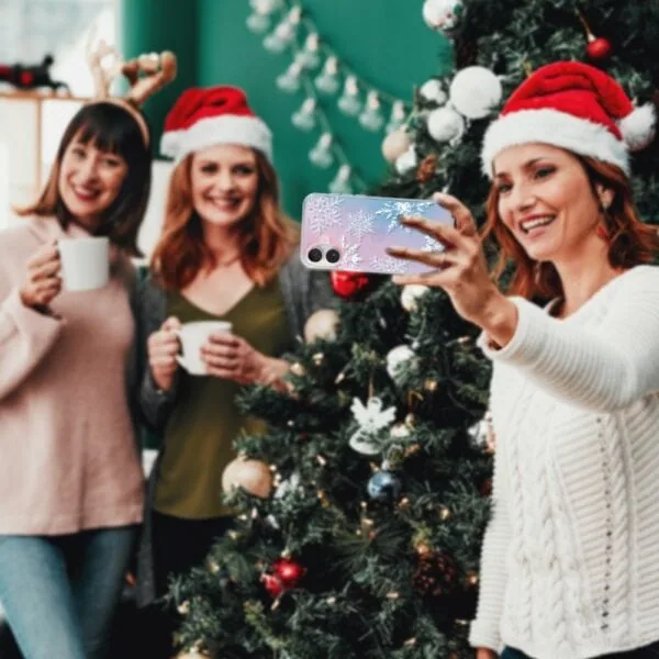 Etui do iPhone 16 Christmas, płatki śniegu, zmieniające kolor (1) Kobiety robią selfie przy choince świątecznej.
