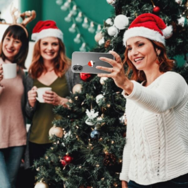 Etui do iPhone 16, czapka Mikołaja (1) Kobiety robią selfie przy choince świątecznej.